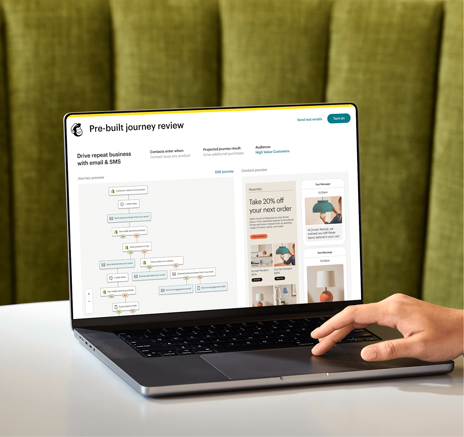 Image of a person sitting at a desk, looking at a laptop screen displaying Mailchimp’s Pre-built journey review feature. The feature shows a preview of an automation journey and an abstract view of email and SMS interfaces from the fictitious brand Assembly.