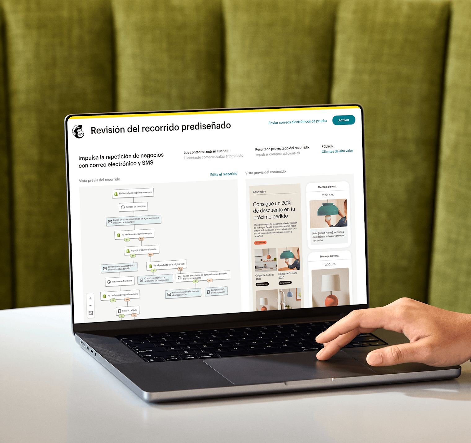 Imagen de una persona sentada frente a un escritorio y mirando la pantalla de una computadora portátil, donde se muestra la función de revisión del recorrido prediseñado de Mailchimp. La función muestra una vista previa de un recorrido de automatización y una vista abstracta de las interfaces de correo electrónico y SMS de la marca ficticia Assembly.